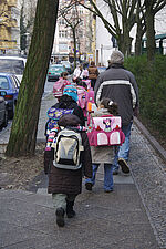 Eine Gruppe Kinder auf dem Weg zur Grundschule. Sie werden von einem Erwachsenen begleitet