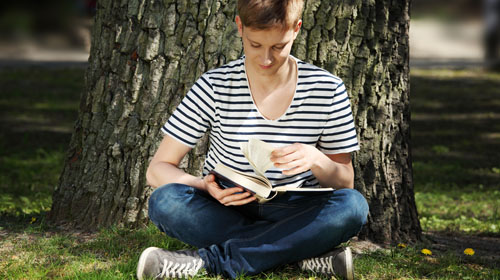Eine Person sitzt unter einem Baum und liest