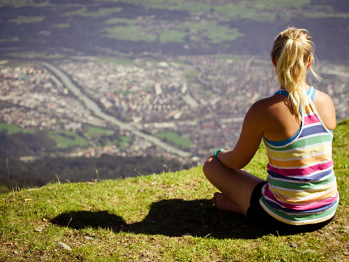 Eine junge Frau sitzt auf einer Anhöhe und blickt auf eine Stadt im Tal herab