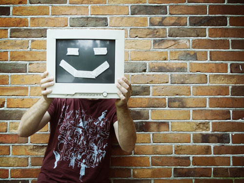 Ein Mann hält sich einen Computermonitor mit aufgeklebtem Smiley vor das Gesicht